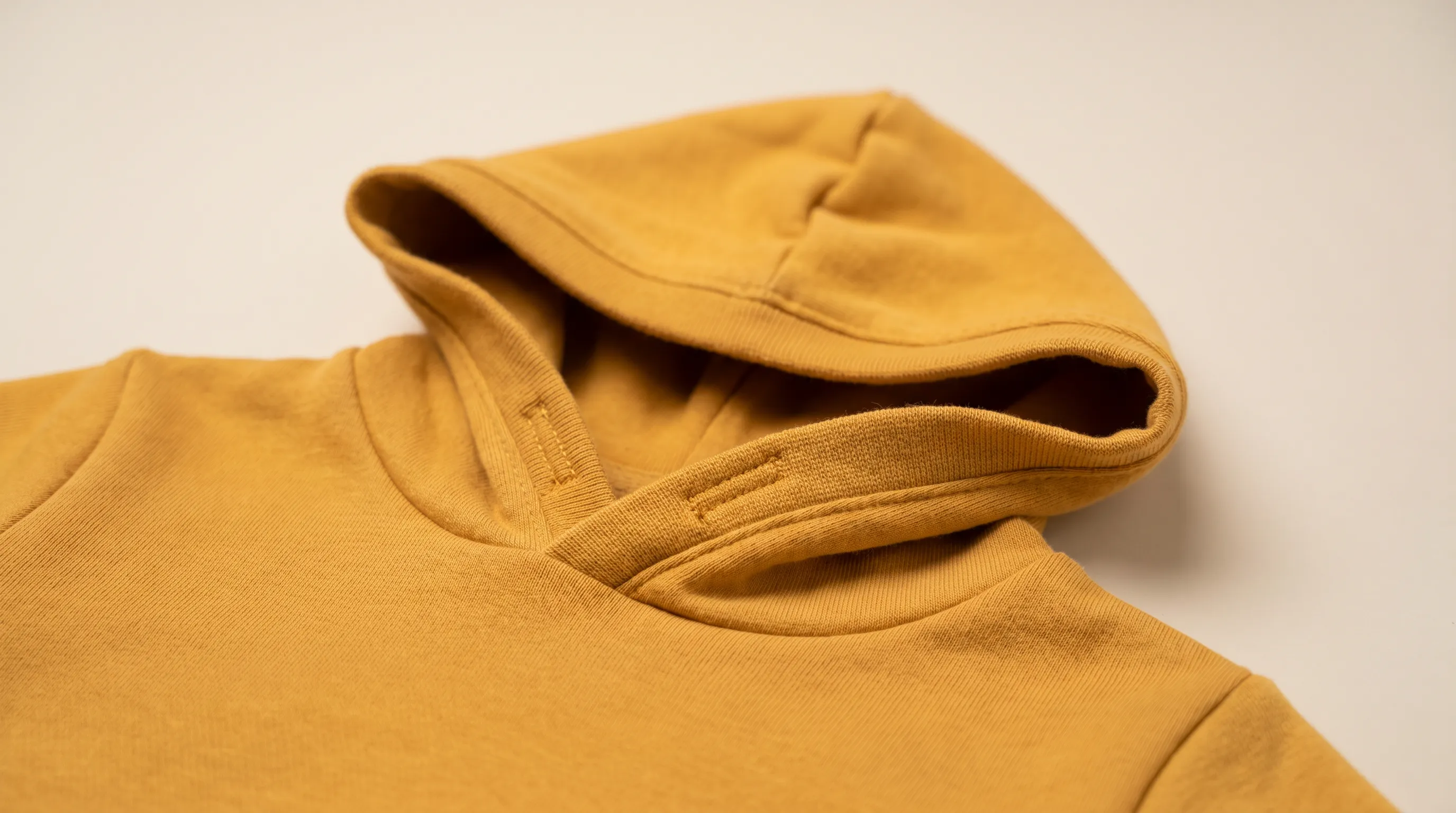 Close-up of a children's hooded sweatshirt hood opening finished with soft covered elastic instead of a drawstring, beside a flat tech-pack page noting the no-drawstring substitution