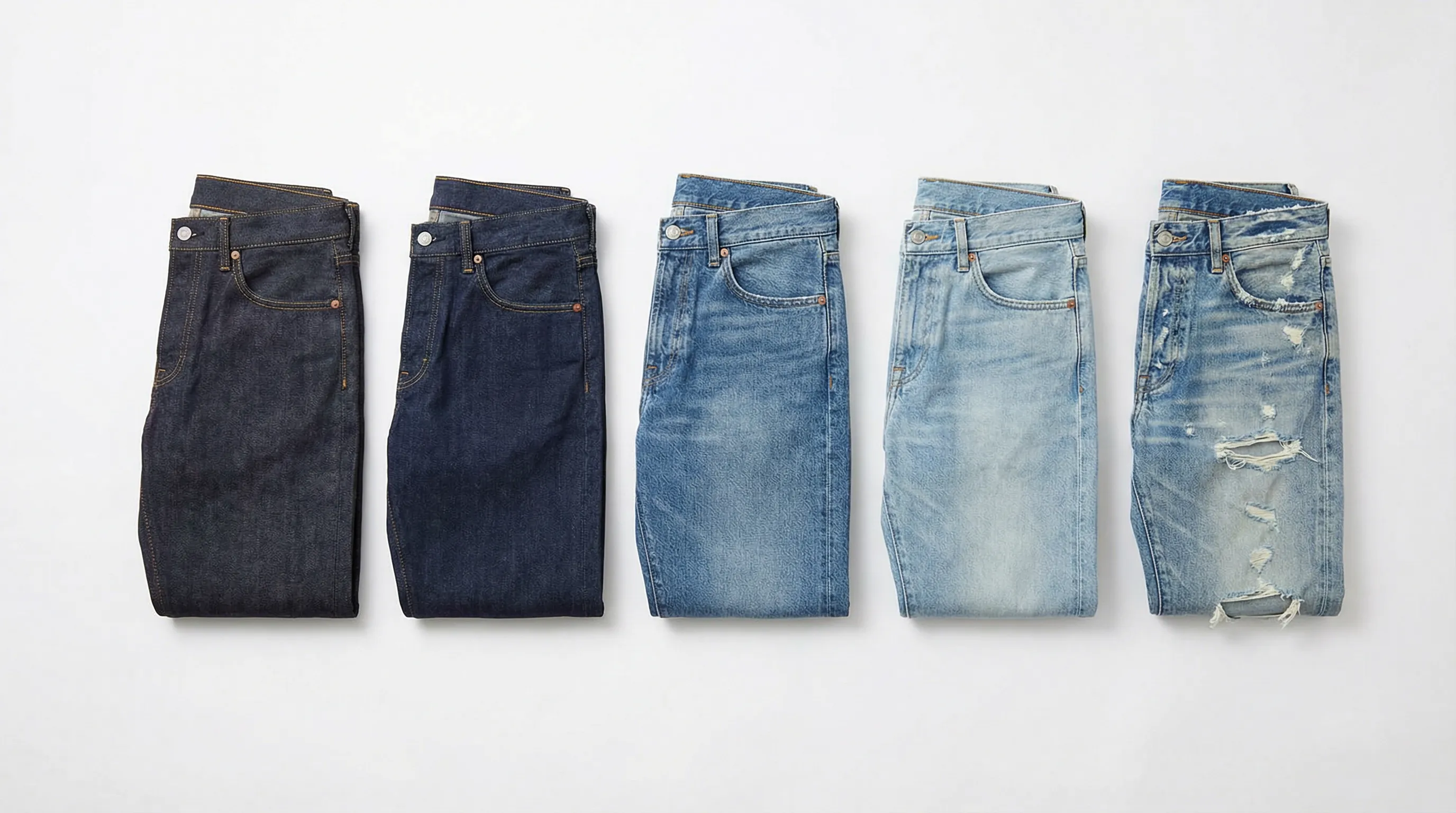 Five pairs of denim jeans showing progressive wash treatments from raw indigo to heavy stone wash to distressed