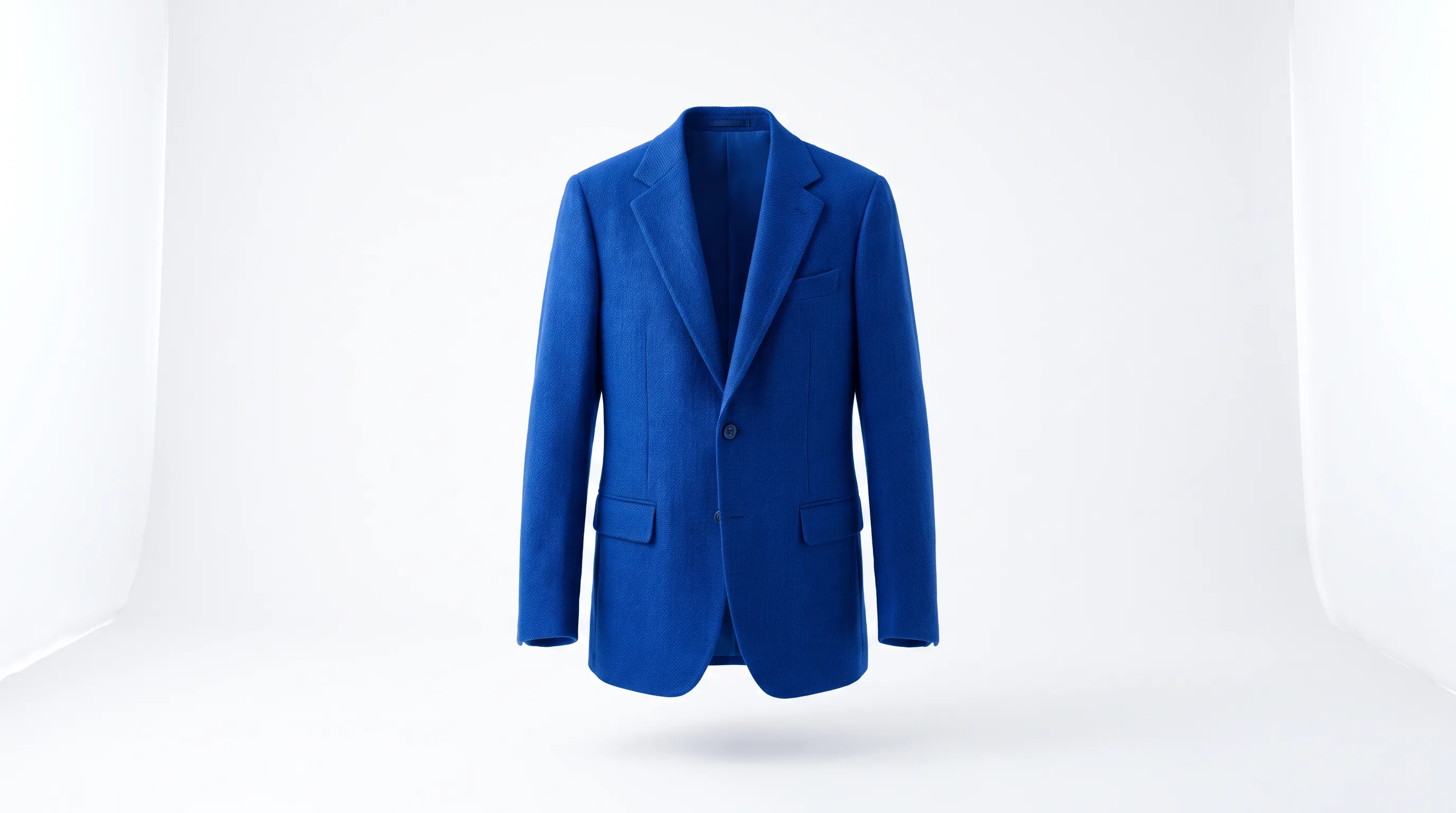 A single tailored blazer hung on a bone-white studio wall under a hard raking light, a sculptural hero product image