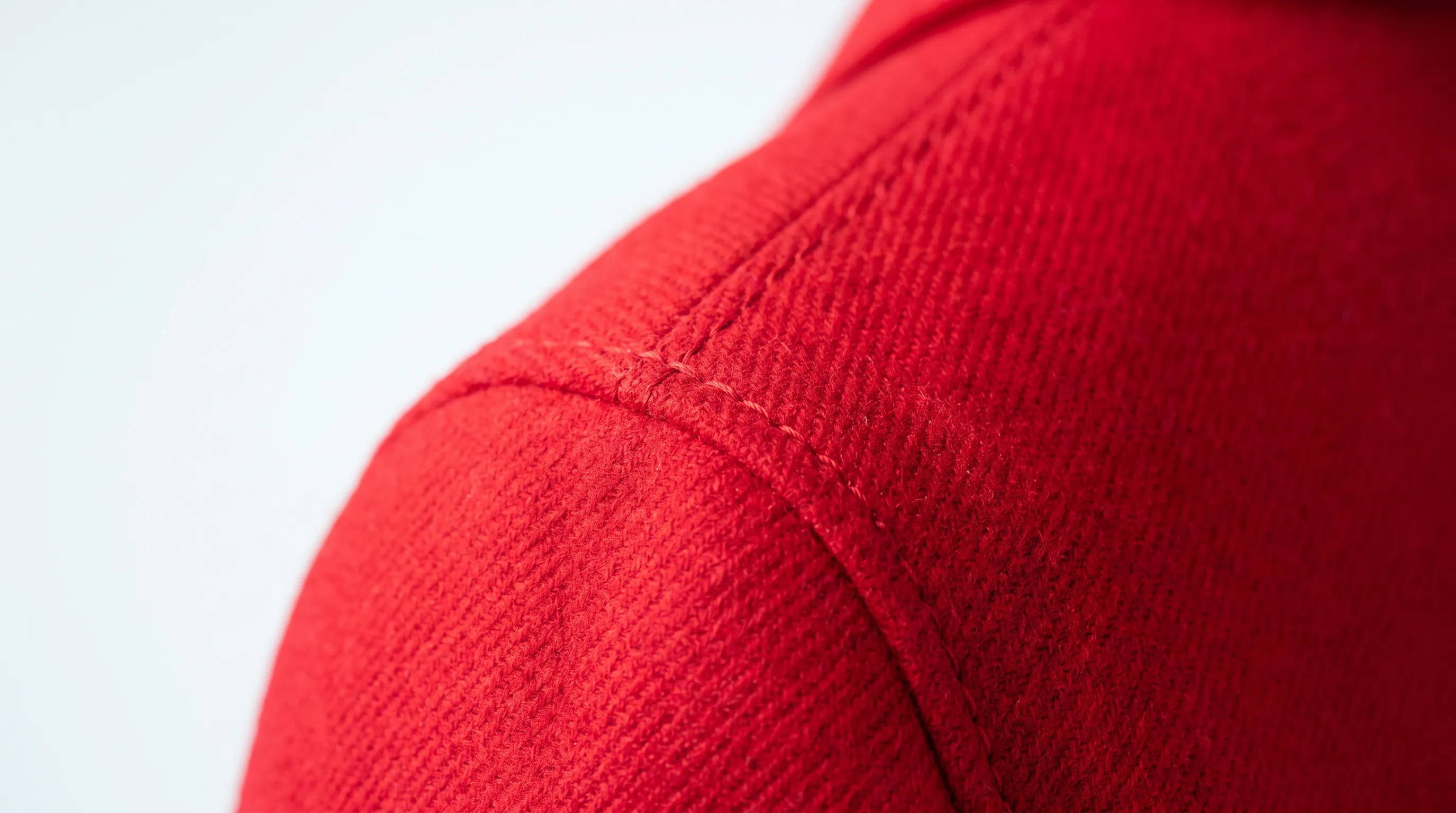 A macro detail of a wool-blend sleeve seam under raking light, showing stitch, weave, and fabric hand