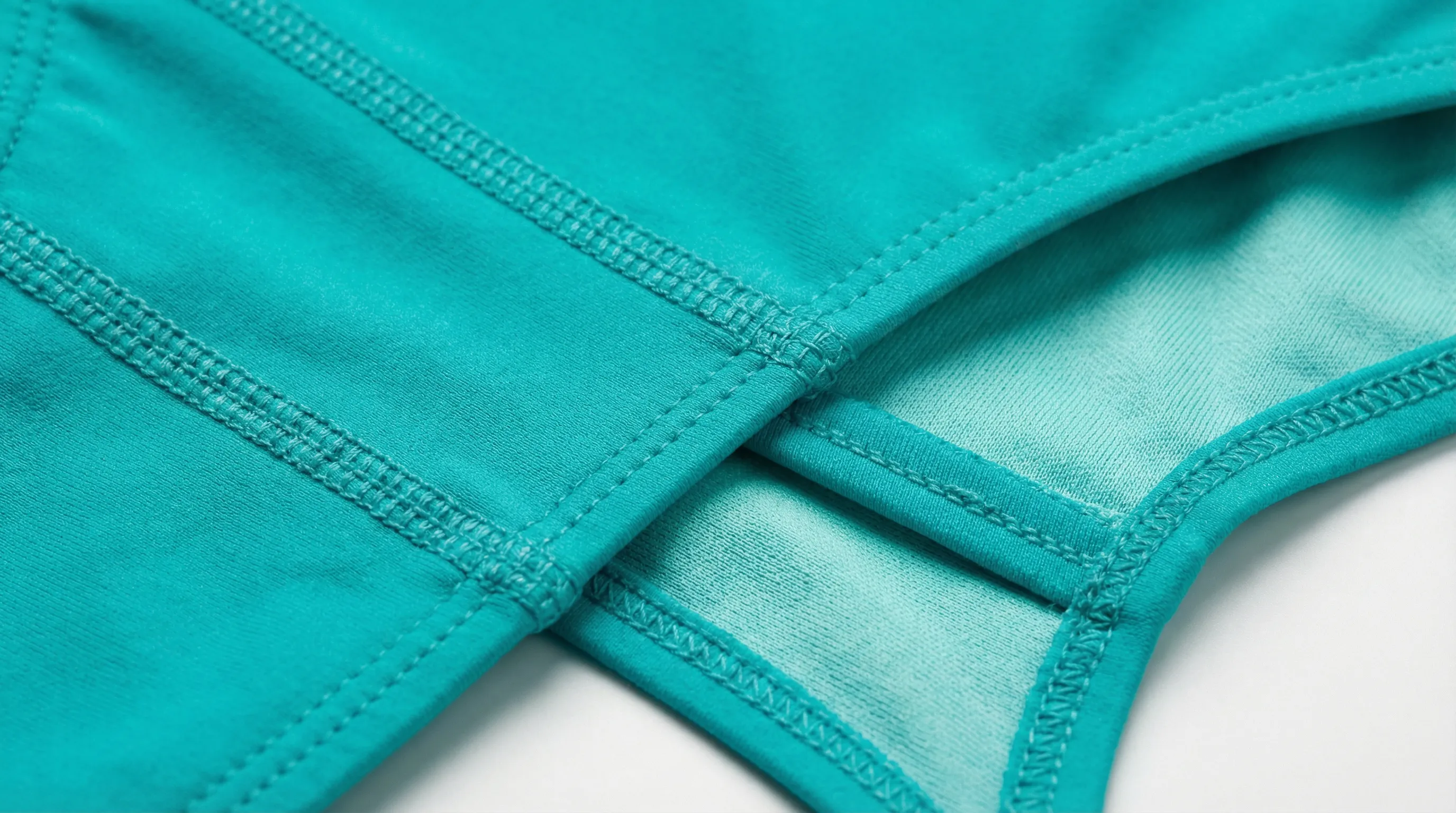 Close-up of swimwear construction showing flatlock seams, fold-over elastic edge finishing, and lining attachment on a bikini bottom